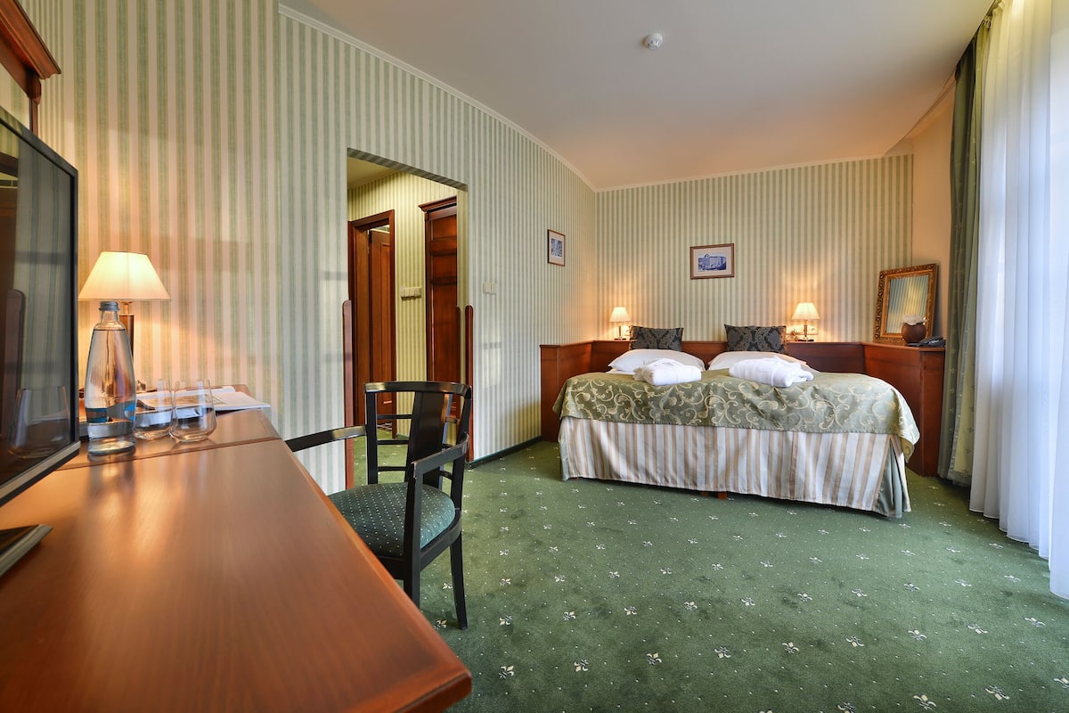 A hotel room with a bed, a desk, and a chair. There is a door leading to another room.