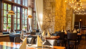 A restaurant with wooden tables, stone walls, and hanging lights. - Golf hotel Morris (Marianske Lazne)