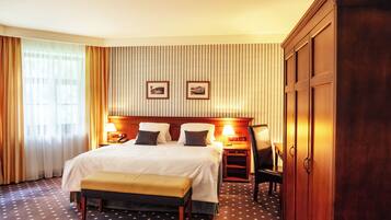 A hotel room with a large bed, bedside tables, a desk, a chair, a wardrobe, and two framed pictures on the wall.