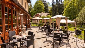 An outdoor patio with wicker furniture, umbrellas, and a view of a forested area. - Golf hotel Morris (Marianske Lazne)