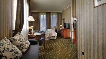 A hotel room with a bed, a sofa, a desk, a television, and a lamp.