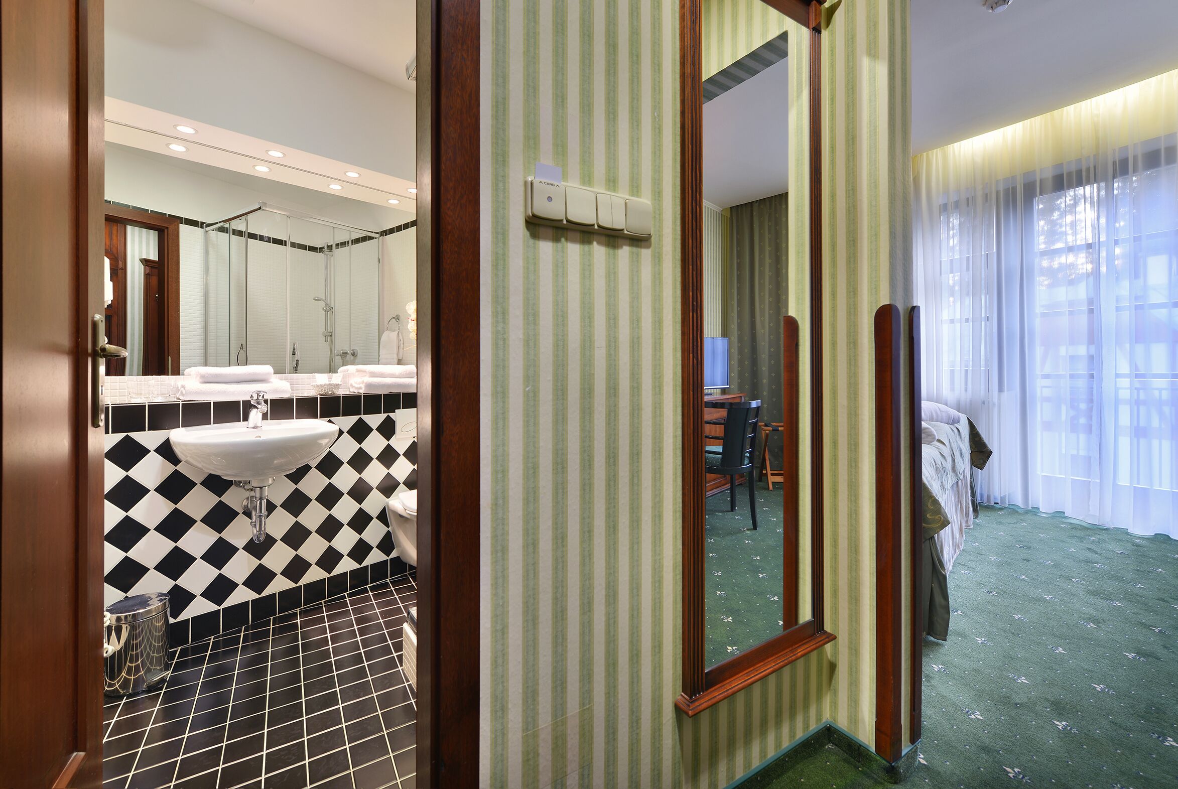 A hotel bathroom with a black and white checkered floor, a sink, and a shower.
