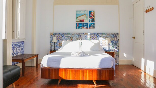 Un dormitorio con cama de madera, una mesita, una silla y una pared decorada con motivos náuticos.