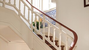 Una escalera con balaustres blancos y barandilla de madera, que conduce a un rellano con vista a una habitación con ventana y puerta.