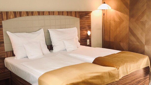 A hotel room with a bed, a nightstand, a wall-mounted lamp, and a patterned floor.