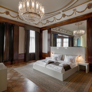Une chambre spacieuse avec un grand lit, de magnifiques lustres décorant le plafond et un grand miroir.