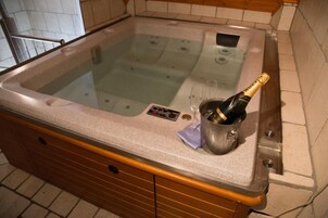 A hot tub with a bottle of champagne and glasses on the countertop.