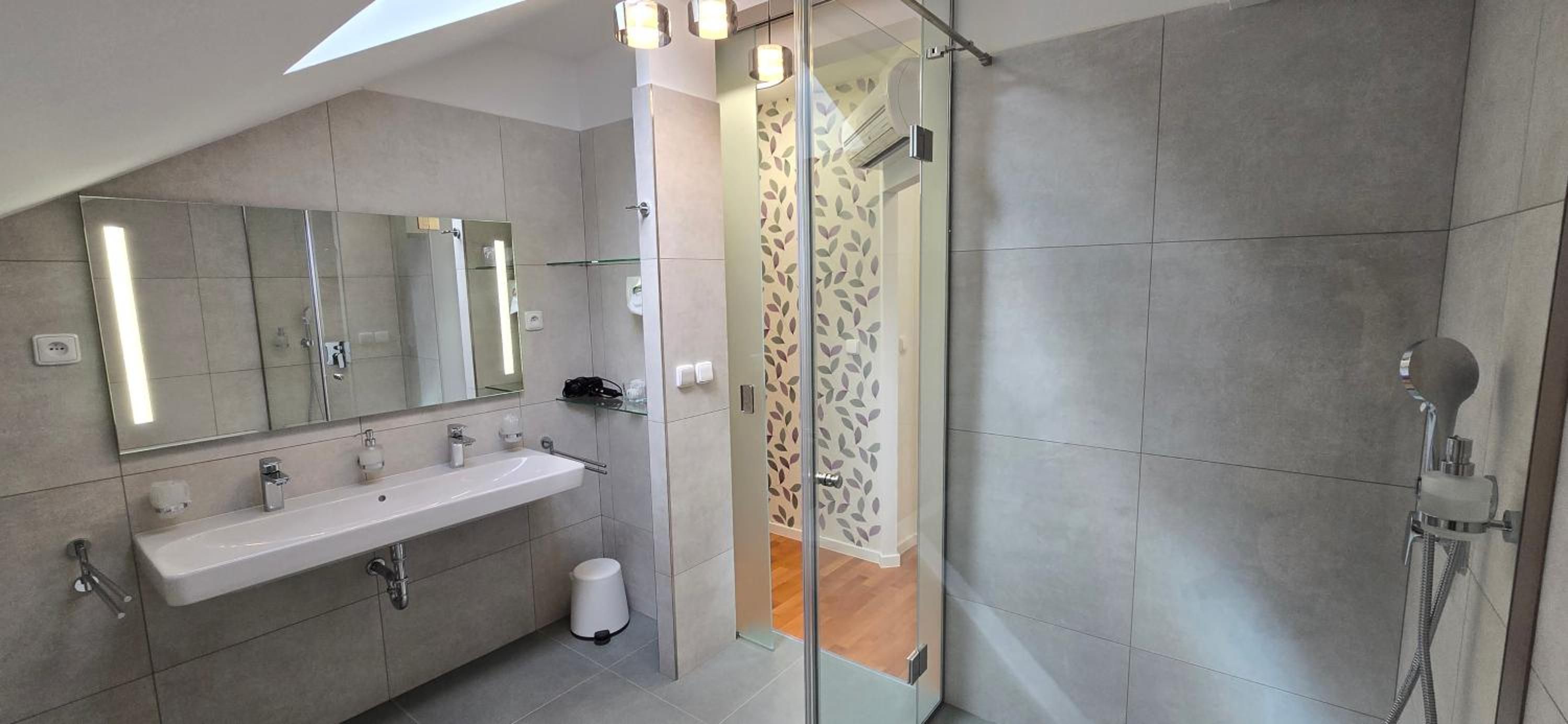 Un baño moderno con tragaluz, un espejo grande, ducha y retrete.