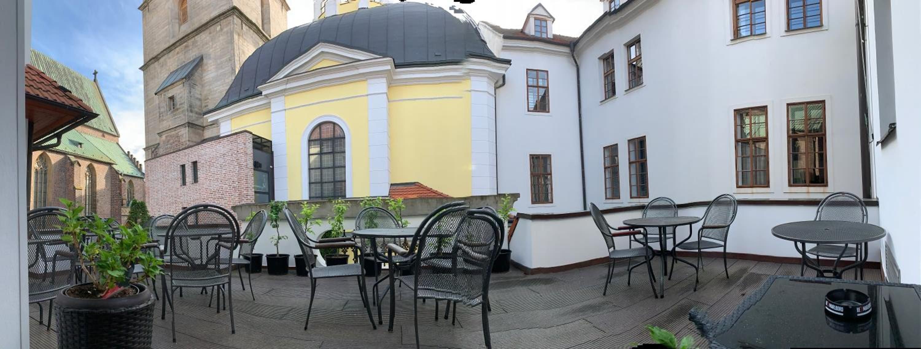 An outdoor seating area with metal chairs and tables, surrounded by buildings with distinct architectural styles.