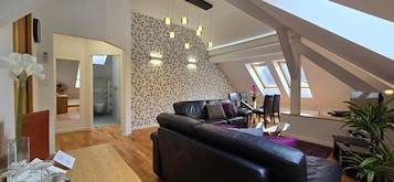 Una sala de estar moderna con un sofá de cuero negro, una mesa de centro de vidrio y un comedor con una mesa y sillas. Hay una escalera que lleva a un nivel superior con tragaluces.