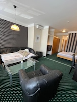 Habitación de hotel con una cama, un sofá, una mesa de centro de vidrio y una silla. Hay un cuadro en la pared y un equipo de aire acondicionado.