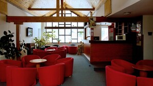 A room with red chairs and tables, wooden beams on the ceiling, a window with plants, and a counter with a microwave. - Hotel Harrachov Inn (Harrachov)