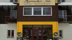 A two-story Harrachov Inn hotel with a yellow and brown facade, large windows, and a snow-covered entrance. - Hotel Harrachov Inn (Harrachov)