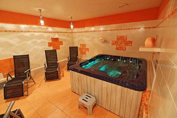 Un cuarto de spa con un jacuzzi, dos sillas, un taburete pequeño y una pared con azulejos decorativos.
