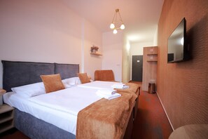 Une chambre d’hôtel avec un grand lit, deux tables de chevet, un téléviseur à écran plat fixé au mur et une petite étagère avec une plante.