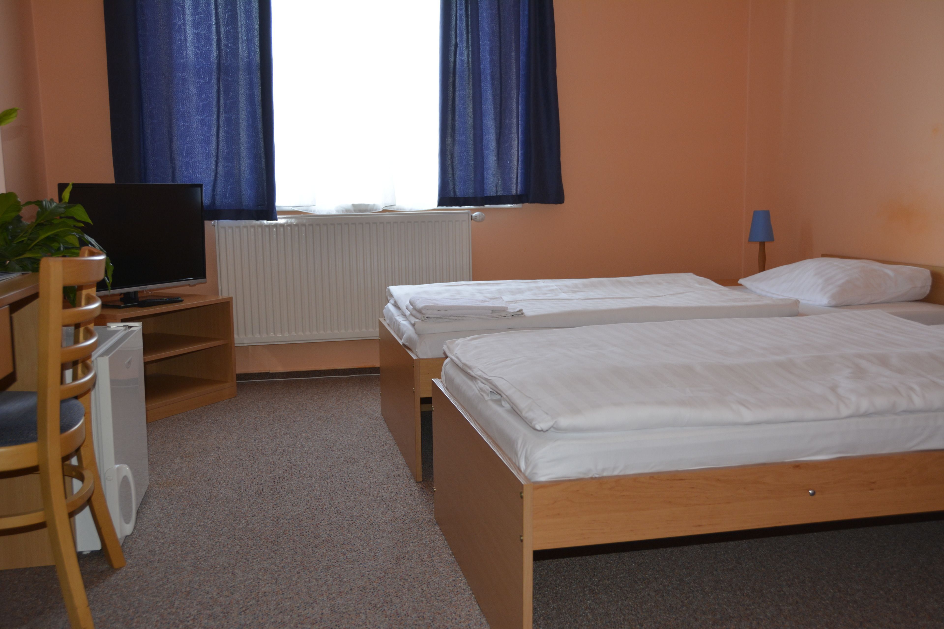 A hotel room with two single beds, a desk with a chair, a television, and a radiator.