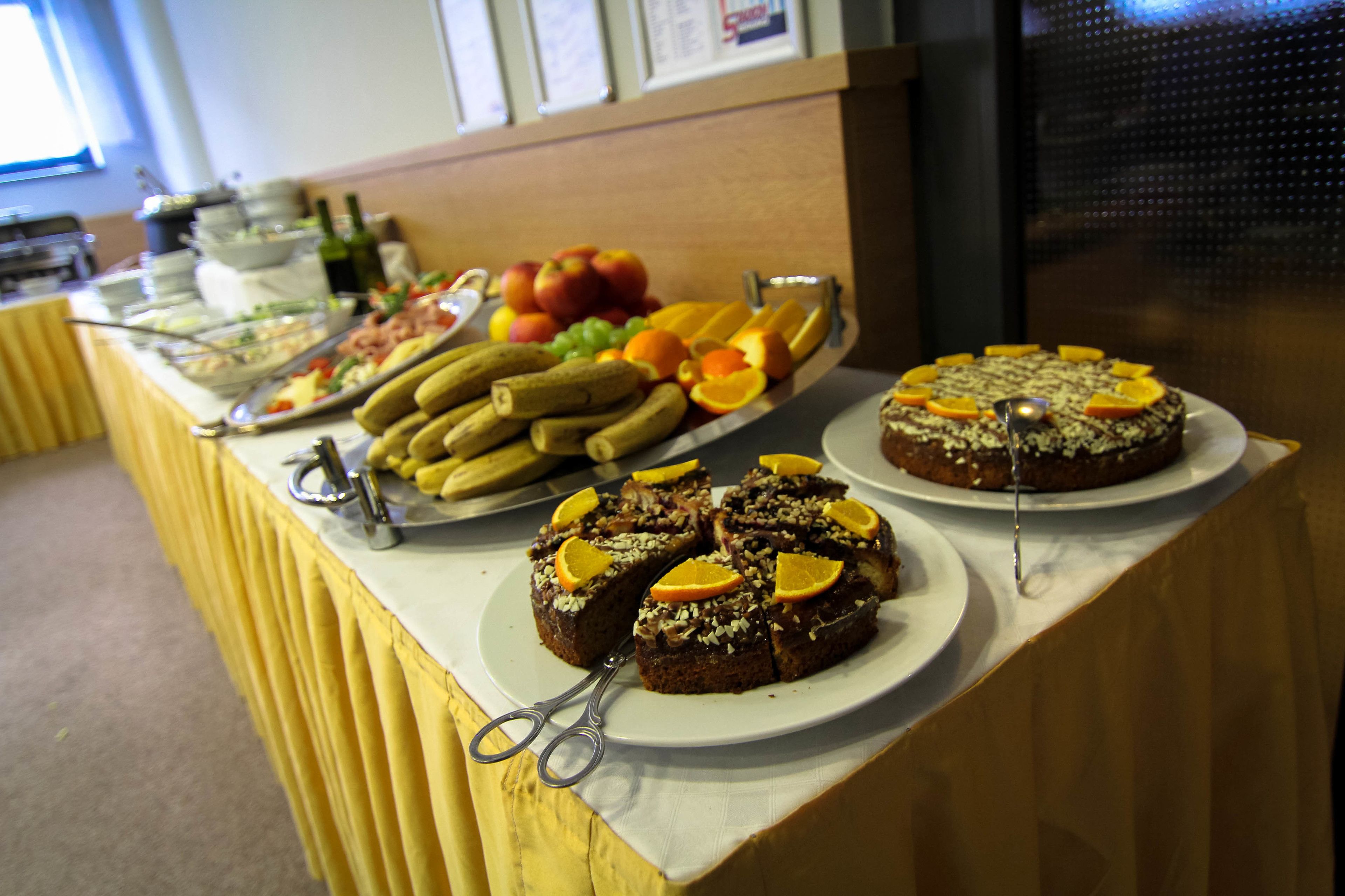 A buffet table with various food items including fruits, vegetables, and a cake.