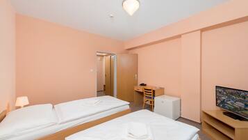 A hotel room with two beds, a desk, a television, and a small refrigerator.