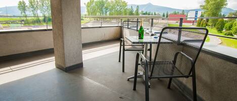 A balcony with a table and chairs, a bottle of champagne, and a view of greenery and buildings.