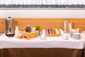 A breakfast buffet setup with a coffee maker, milk jug, condiments, and a variety of tea and coffee packets. - Hotel Arena (Liberec)