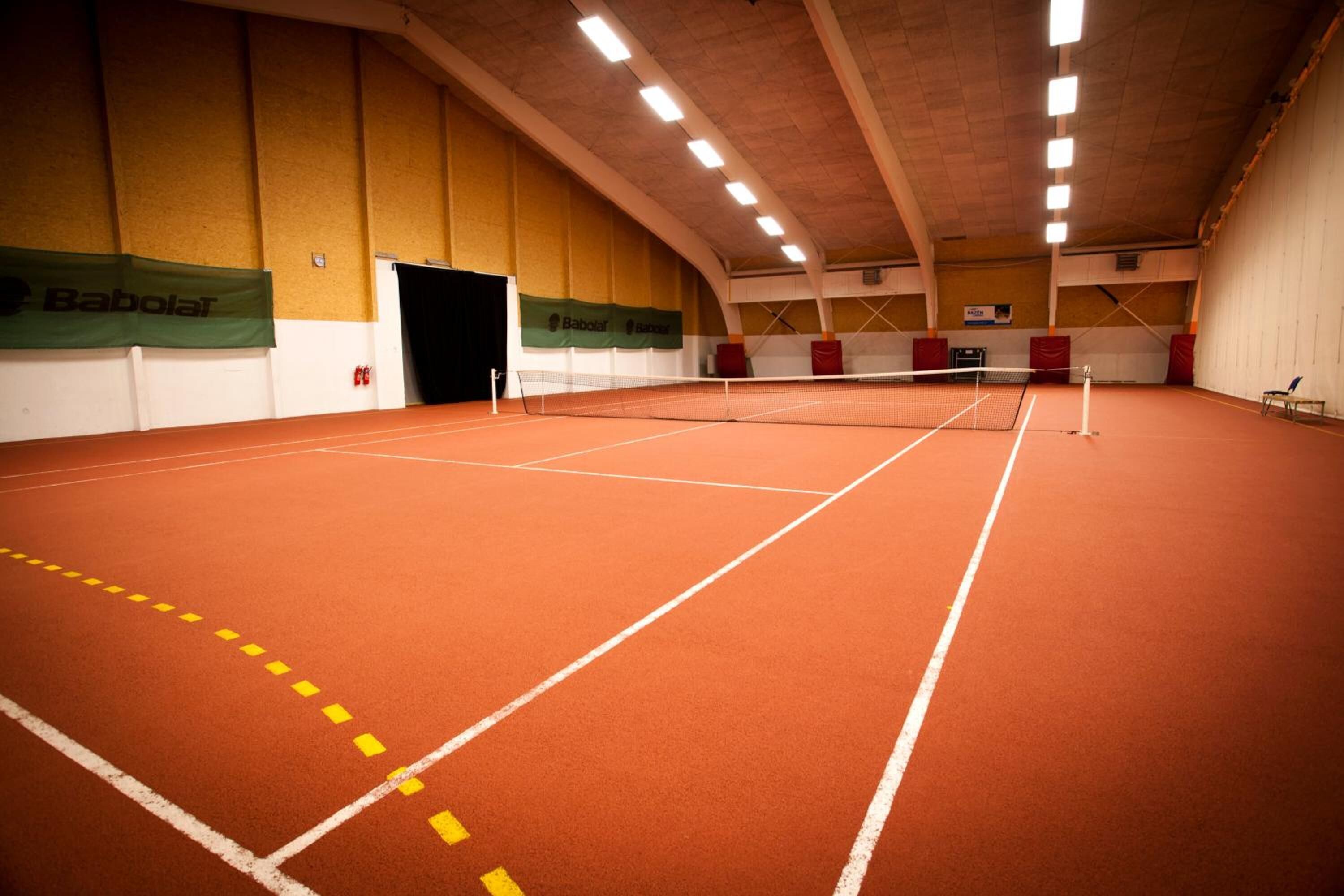 Una cancha de tenis interior con red, paredes y una puerta.