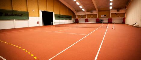 Una cancha de tenis interior con red, paredes y una puerta.