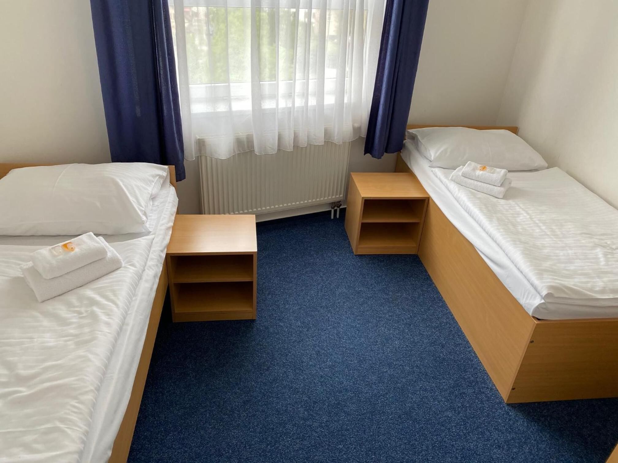 Een kleine, schone kamer met twee bedden, een nachtkastje en een raam met gordijnen.