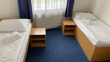 Een kleine, schone kamer met twee bedden, een nachtkastje en een raam met gordijnen.