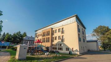 A multi-story building with a playground in front, a clear sky, and a paved area.