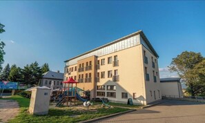 A multi-story building with a playground in front, a clear sky, and a paved area. - Hotel Petra (Liberec)