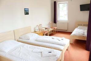 Une chambre d’hôtel avec deux lits simples, une petite table avec une chaise, une fenêtre avec des rideaux et un téléviseur fixé au mur.