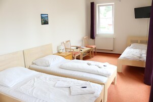 Una habitación de hotel con dos camas individuales, una mesita con una silla, una ventana con cortinas y un televisor en la pared.