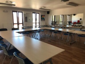 Une salle de classe avec de longues tables et des chaises, une grande fenêtre et un radiateur.