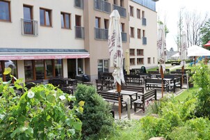 Un área de estar al aire libre con mesas y sillas, rodeada de vegetación y un edificio con múltiples ventanas y balcones.
