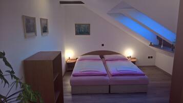 A bedroom with a large bed, two bedside tables with lamps, a wooden bench, and framed pictures on the wall.