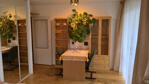 A room with a wooden dining table, chairs, a cabinet with glass doors, and a large potted plant.