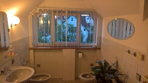 A bathroom with two sinks, a toilet, a window with blinds, a mirror, and a potted plant. - Privat Apartma Ulrych (Liberec)