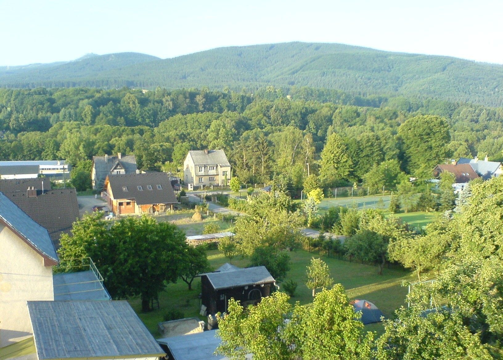 A residential area with houses, a tennis court, and a forested hill in the background.