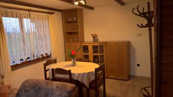 Una zona de menjador amb una taula rodona, cadires, un vas amb flors, un moble de fusta i una finestra amb cortines.