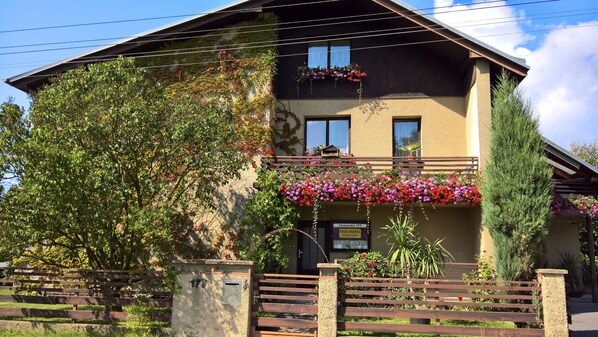 A two-story building with a balcony adorned with flowers, a stone gate, and a sign indicating the property name and room number. - Privat Apartma Ulrych (Liberec)