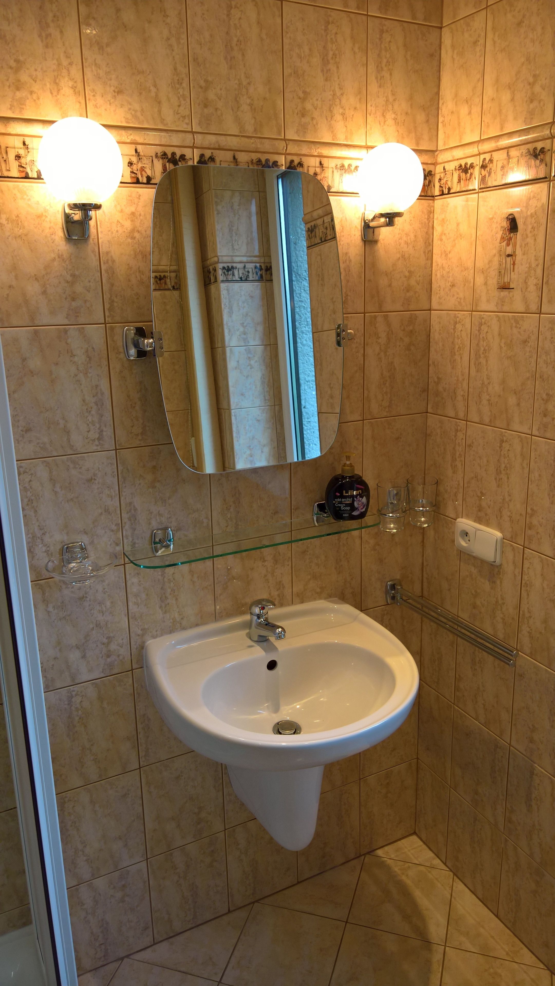 A bathroom with a white sink, a glass shelf with toiletries, and a wall-mounted mirror.