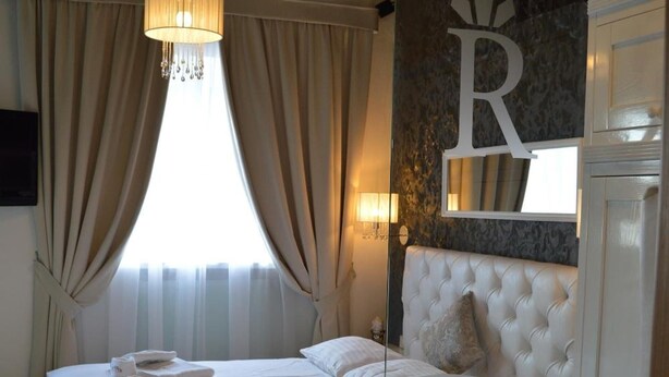 Habitación de hotel con una cama grande, un candelabro, un espejo y la letra 'R' colgada en la pared.