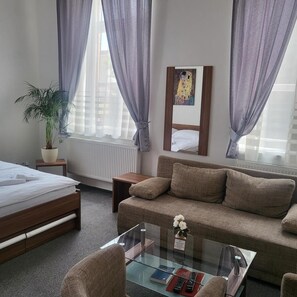 Una camera d'albergo con un letto, un divano, un tavolino in vetro, un piccolo comodino, una pianta in vaso e un quadro appeso al muro.