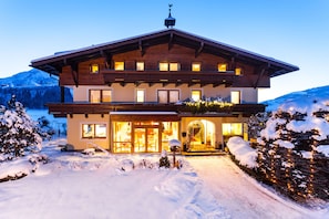 A large, multi-story wooden building with a sloped roof, large windows, and a well-lit entrance. - Pension St. Georg (Kaprun)