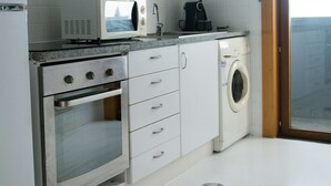 Eine kompakte Küche mit weißen Schränken, einer Mikrowelle, einer Kaffeemaschine, einem Backofen und einer Waschmaschine.