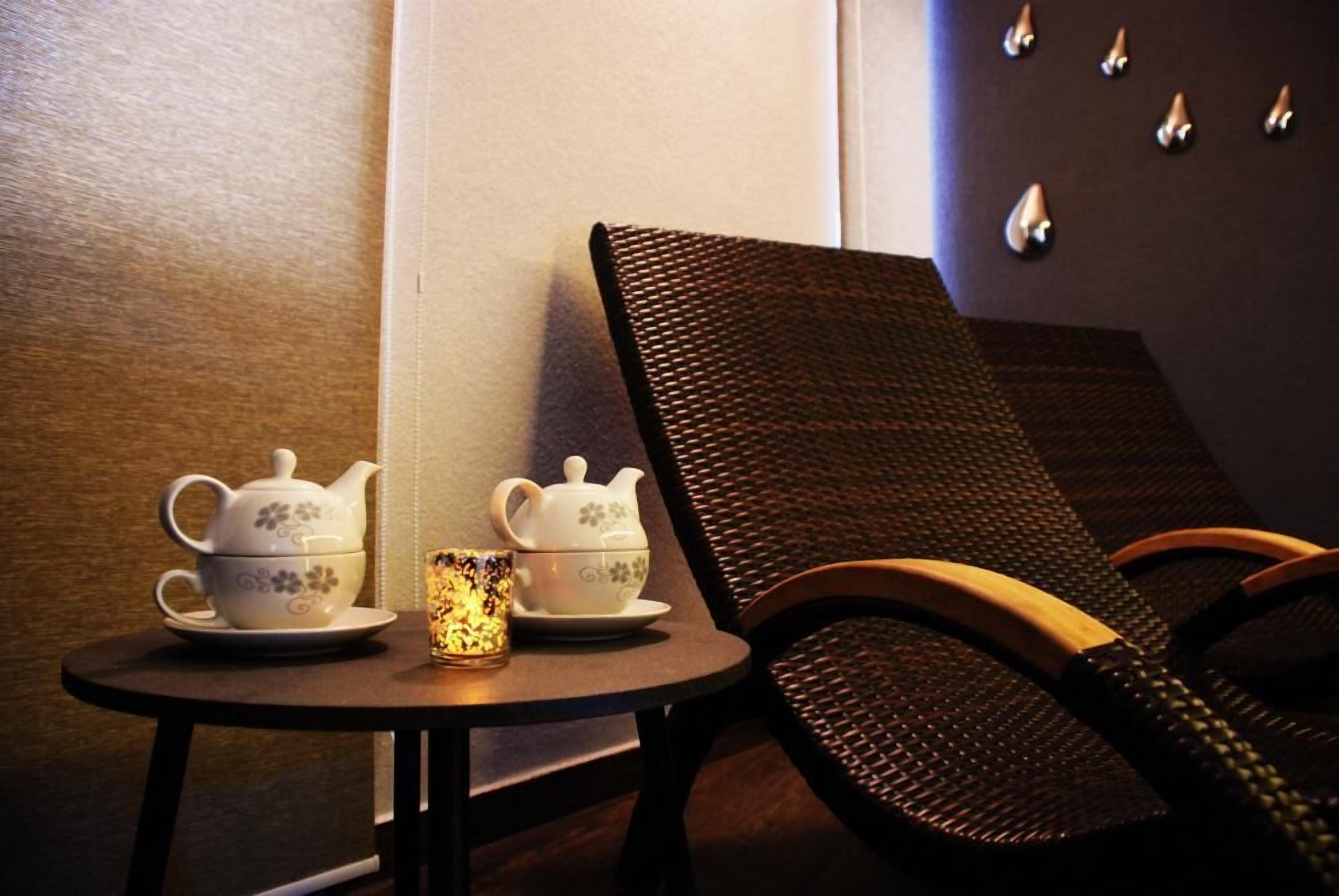 A small table with two teapots and a cup, a chair, and a wall with decorative elements.