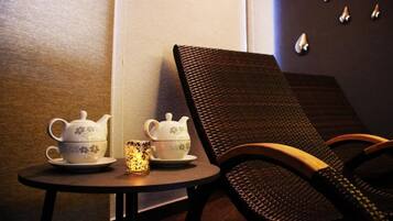 A small table with two teapots and a cup, a chair, and a wall with decorative elements.