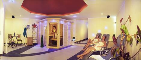 Un área de spa con sauna de madera, sillones de masaje y una pequeña mesa con sillas.