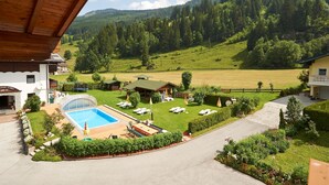 A hotel with a swimming pool, a tennis court, and a view of a green valley and forested hills. - Pension Anja (Kleinarl)