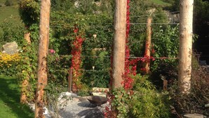 A garden with wooden posts and wire fencing, surrounded by greenery and flowers. - Pension Anja (Kleinarl)